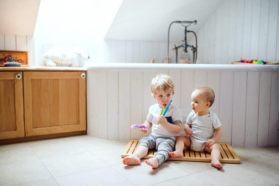 a toddler and baby sitting on a bathroom floor with a toothbrush