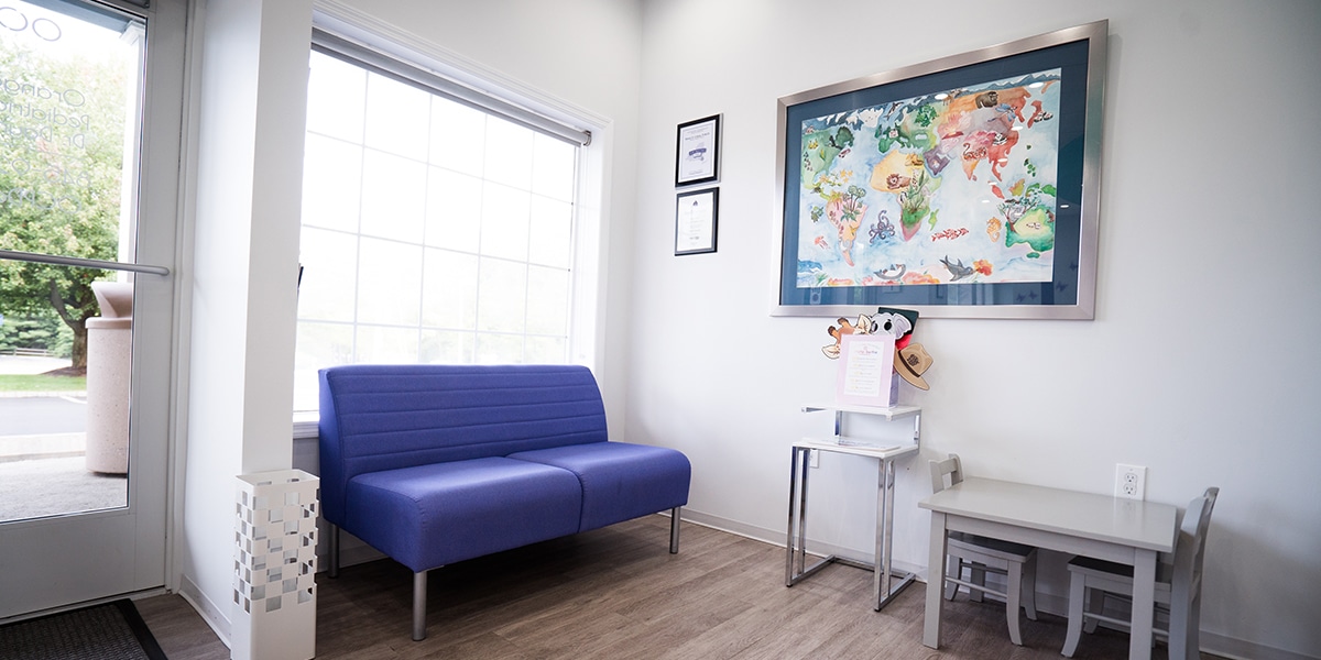 purple love seat by window and small grey table with chairs in dental office waiting room